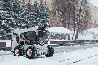 A skid-steer clearing snow along a commercial building